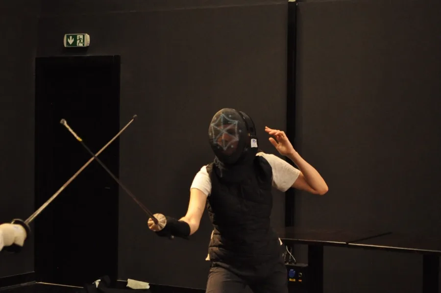 A fencer in a mask and jacket counterattacking in a training hall